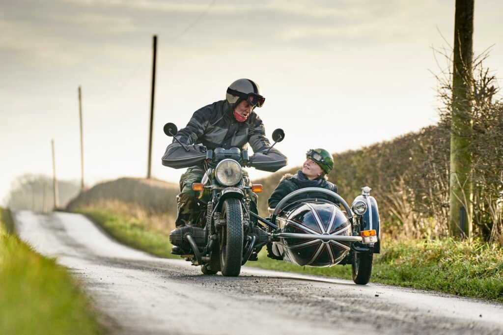 Senior man and grandson riding motorcycle and sidecar along rural road